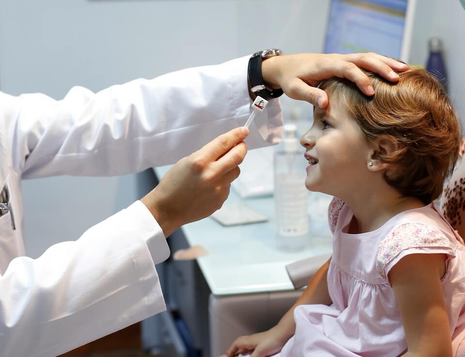 Niño en revisión ocular con optotipo, destacando la importancia de la revisión visual anual tras las vacaciones.